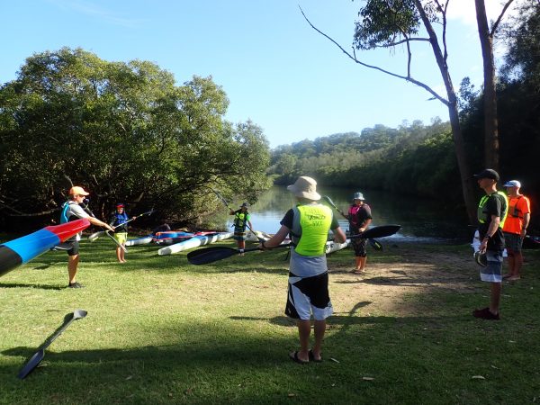 Our coach standing on the left of a circle of novice paddlers practicing their stroke